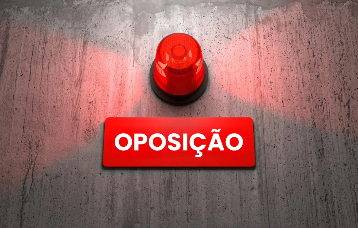 Imagem de uma luz de alerta vermelha sobre um fundo cinza com uma placa escrita "OPOSIÇÃO" em destaque, simbolizando desafios da oposição no registro de marca.